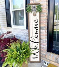 a wooden sign that says welcome hanging on the side of a house with potted plants next to it