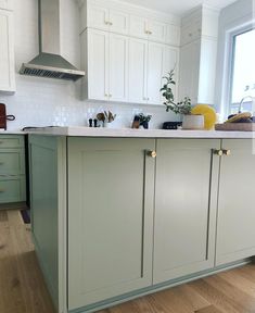 a kitchen with green cabinets and white counter tops, along with wooden floors in front of a window