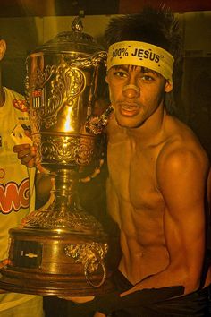 two shirtless men holding up a trophy in front of their face and one has his headband on