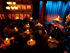 a group of people sitting at tables in a room with blue curtains and lights on the walls