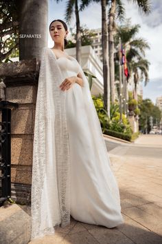 a woman wearing a white wedding gown standing next to a pole with palm trees in the background