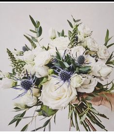 a bouquet of white flowers and greenery is held by someone's hand in front of a wall