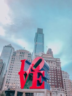 the love sculpture in front of skyscrapers is red, green, blue and black