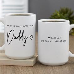 two white coffee mugs sitting on top of a wooden table next to each other