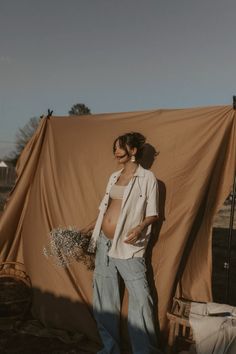 a woman standing in front of a brown tarp with her belly exposed and hands on her hips