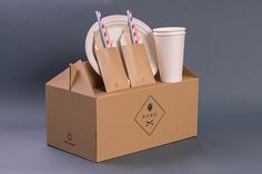 a cardboard box with two cups and plates in it, sitting on a gray surface