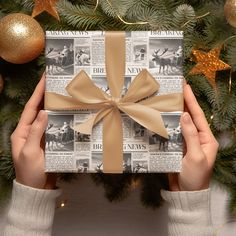 a person holding up a wrapped present in front of a christmas tree with gold ornaments