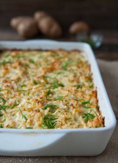 a casserole dish with cheese and herbs in it on a table next to garlic