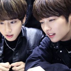 two young men sitting next to each other looking at something on a cell phone in front of them