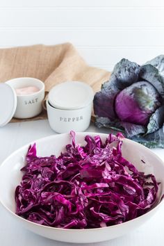 a bowl filled with red cabbage next to some other food items on a white table