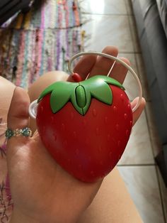 a hand holding a plastic strawberry with a green leaf on it's head and ring around its thumb