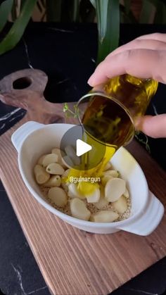 a person pouring oil into a bowl filled with nuts