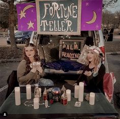 two women sitting in front of a table with candles and signs on it that say fortune teller