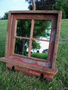 an old window frame sitting in the grass with a tree reflected in it's reflection