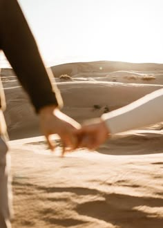 two people holding hands in the sand dunes