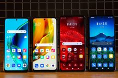 four different phones lined up on top of a wooden table in front of a brick wall