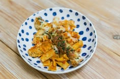 a white and blue bowl filled with pasta on top of a wooden table next to a fork