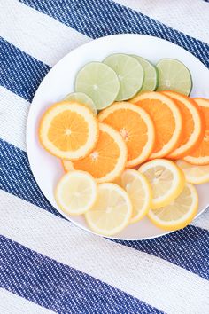 sliced oranges and limes on a white plate with blue and white striped tablecloth