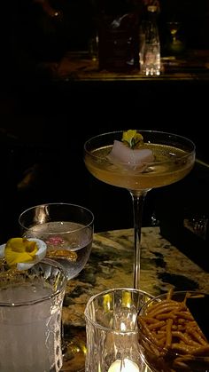 two glasses filled with drinks sitting on top of a table next to some food and candles