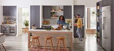 two people in a kitchen preparing food on the counter and standing next to an island with stools