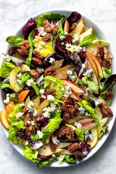 a salad with apples, lettuce and walnuts in it on a white plate