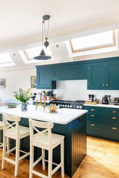 a kitchen with green cabinets and white counter tops, two stools in front of the island