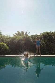 a woman standing next to a swimming pool with a dog in the middle of it