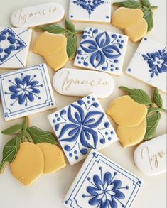 cookies decorated with blue and white designs on a table next to lemons, oranges, and leaves