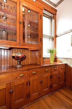 a kitchen with wooden cabinets and glassware on the top shelf, along with a potted plant