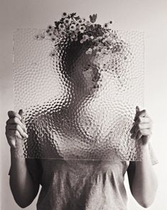 a woman holding up a piece of glass with flowers on it's head in front of her face