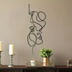 a metal sculpture on the wall above a table with two candles and a potted plant