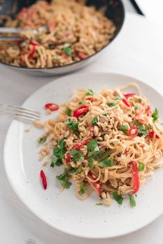 a white plate topped with noodles and veggies next to a frying pan