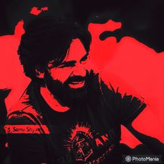 a man with long hair and beard wearing a black t - shirt is smiling in front of a red background