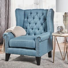 a blue chair sitting on top of a rug next to a table with a lamp