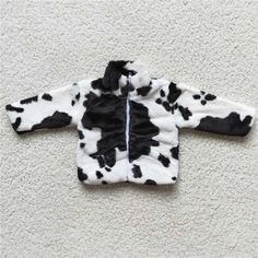 a black and white cow print jacket sitting on top of a carpeted floor next to a wall