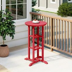 a red table sitting on top of a porch next to a potted plant