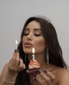 a woman wearing a tiara holding a cupcake with two candles in her hand