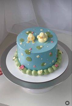 a blue cake decorated with ducks and lily pads on a silver platter in front of a white backdrop