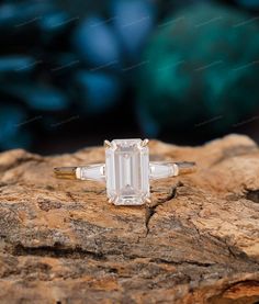 an emerald cut diamond ring sitting on top of a rock