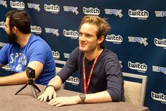 two men sitting at a table in front of a blue wall with the words switch on it