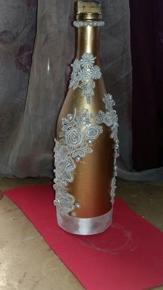 a wine bottle decorated with white lace and flowers on a red mat in front of a curtain