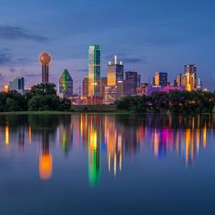 a city skyline is reflected in the water at dusk with colorful lights on it's skyscrapers