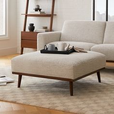 a living room with a couch, coffee table and books on the floor in front of a window