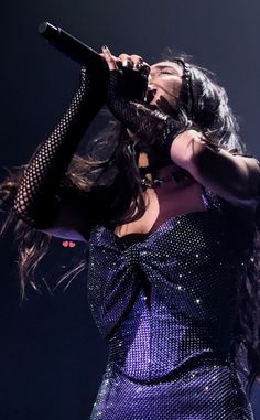 a woman in a purple dress holding a microphone up to her ear and singing on stage