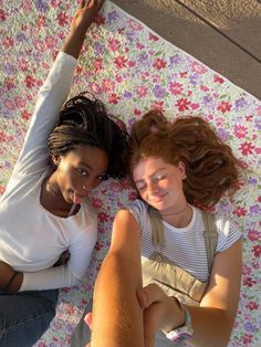 two young women laying on top of a flowered blanket with their arms around each other