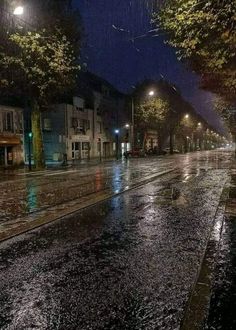 a wet street at night with buildings and trees in the background, it's raining