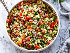 a white bowl filled with cucumber and red onion salad next to two spoons