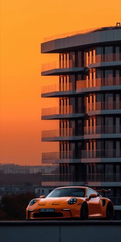 an orange sports car parked in front of a tall building with balconies at sunset