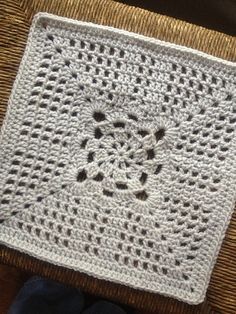 a white crocheted square sitting on top of a wicker floor next to a pair of shoes