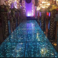 an indoor dance floor with blue lights and white flowers on the bottom, surrounded by candles